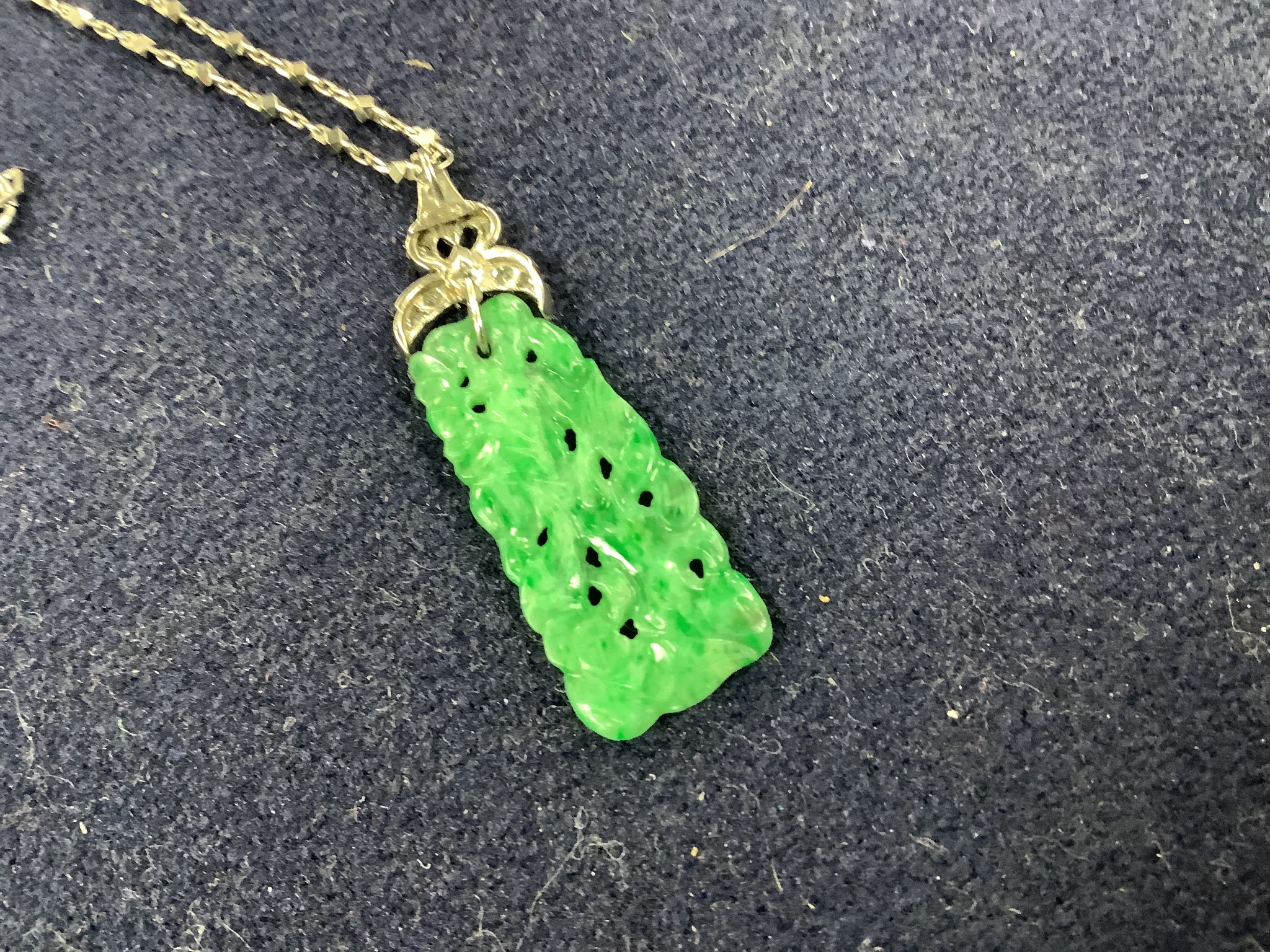 A 1920's white metal and diamond mounted carved jade pendant, numbered 'G 320 1', 4cm, on a platinum fancy link chain, 40cm, gross weight 7.6 grams